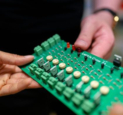 Close-up of hands holding a green circuit board used for electronic projects.